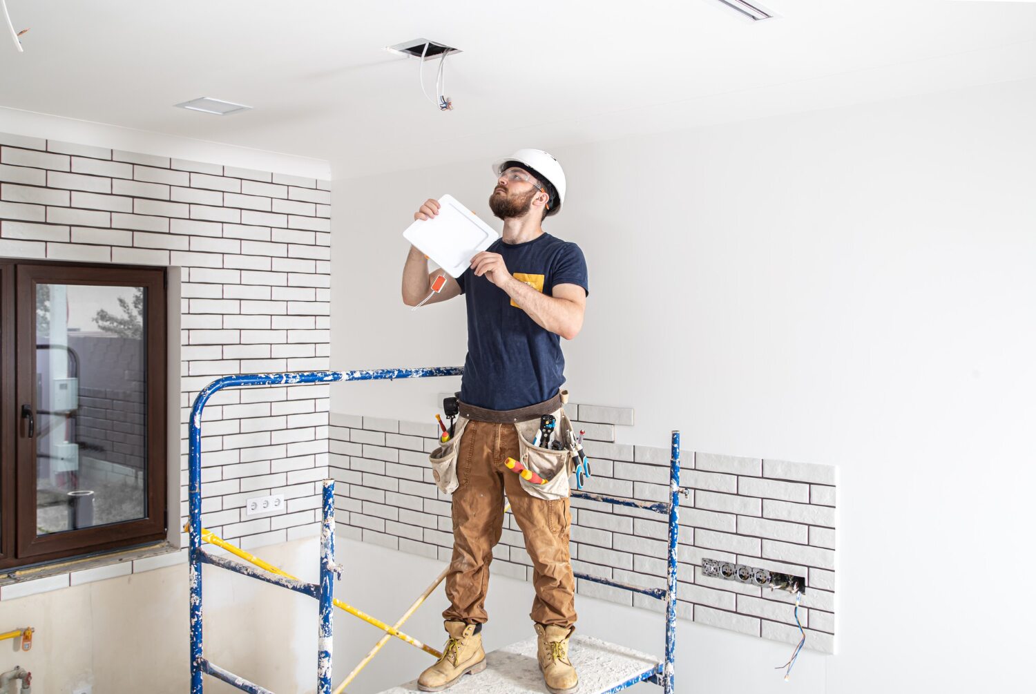 electrician-builder-with-beard-worker-white-helmet-work-installation-lamps-height-professional-overalls-with-drill-repair-site